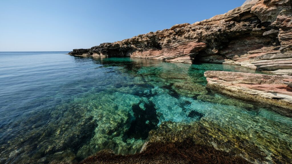A beautiful shot of clear water near a rocky cliff on a sunny day
